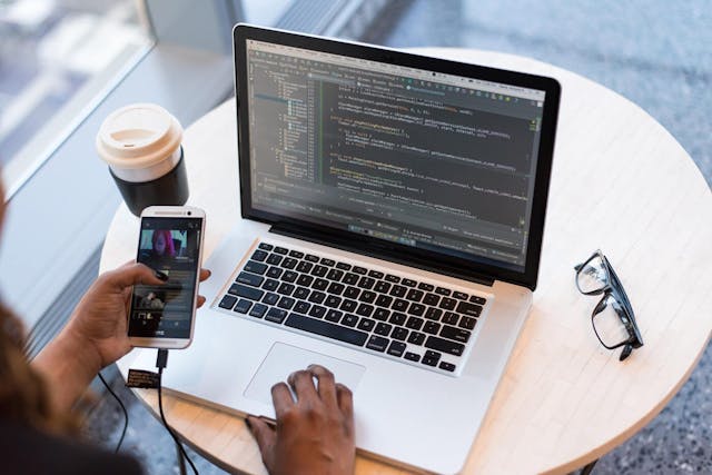 Female programmer multitasking with smartphone and laptop.