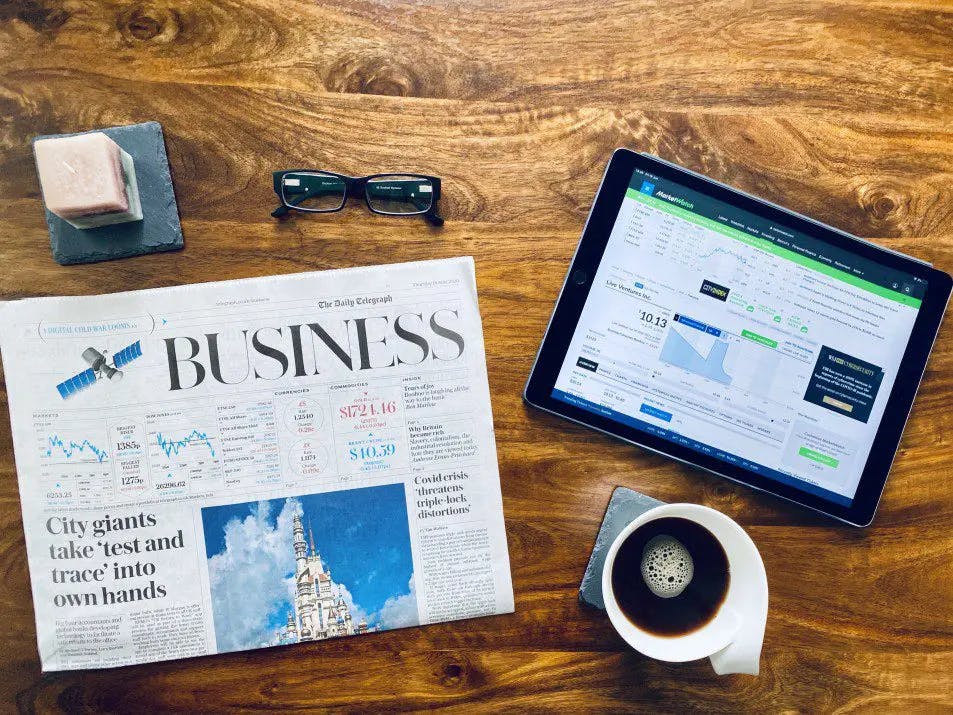 a tablet, glasses and a newspaper on a table