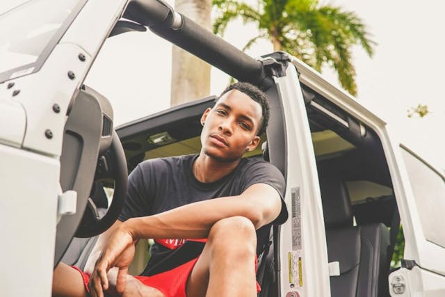 A young man confidently sits in the driver's seat of a car