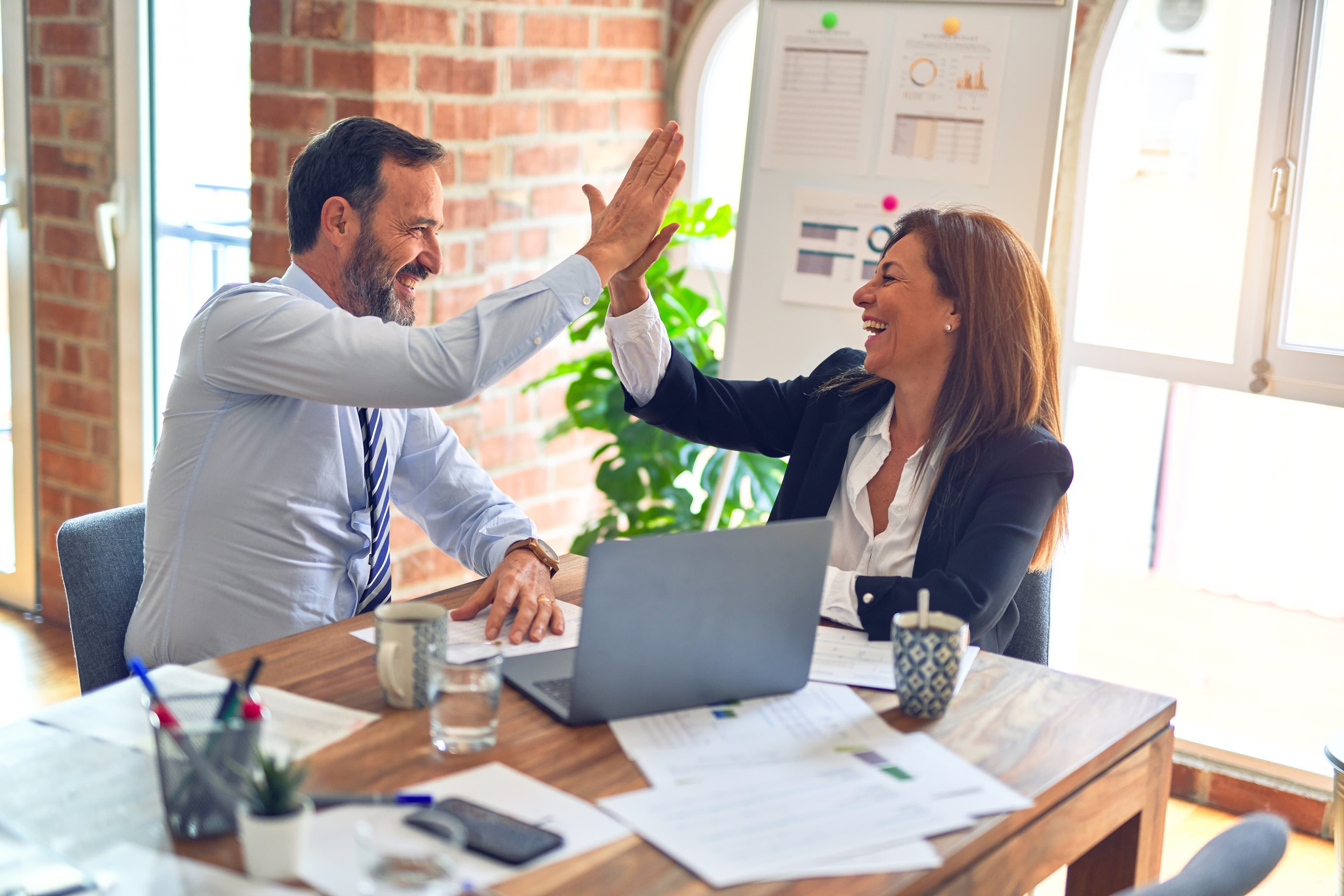 Two professionals celebrate success with a high five at a desk, showcasing teamwork and achievement.