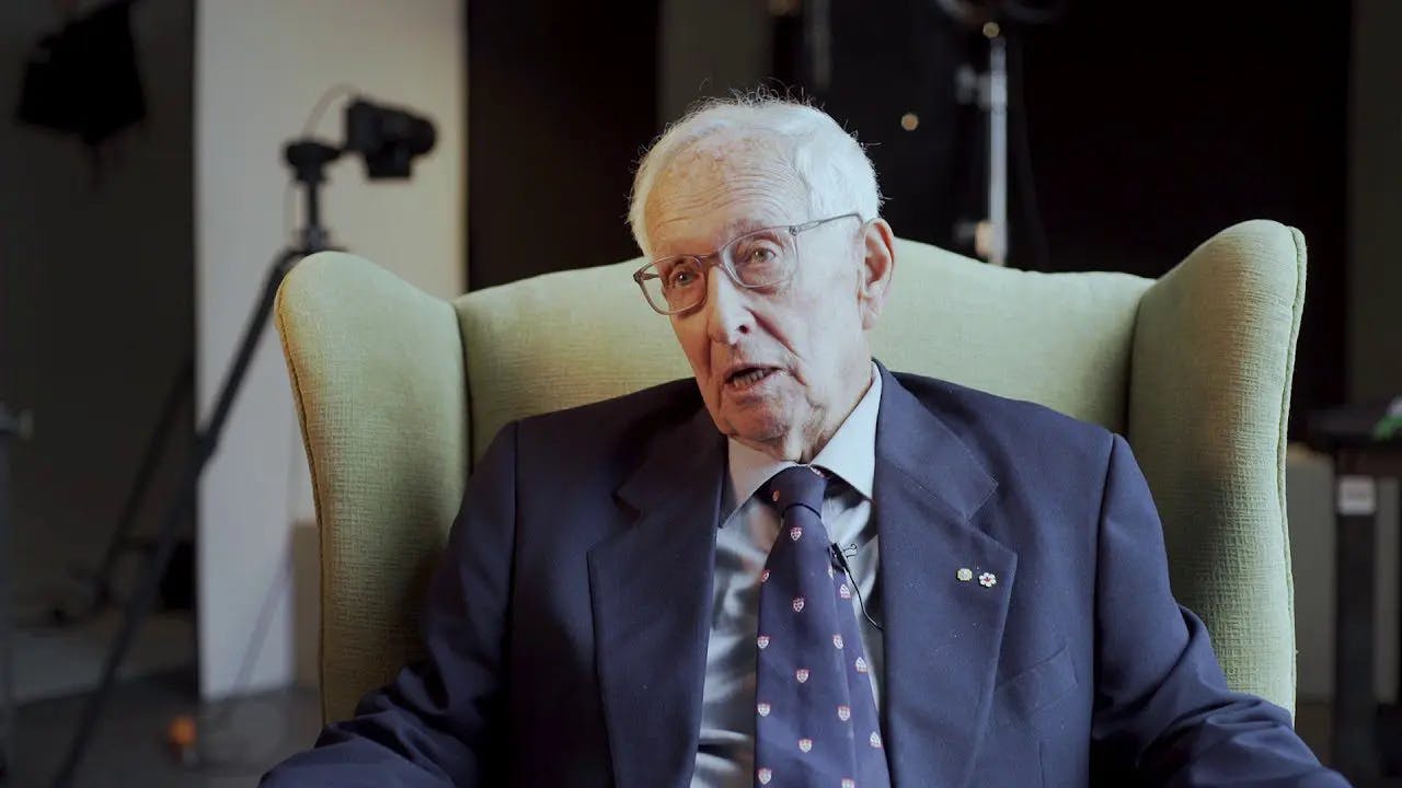 An elderly gentleman in formal attire, seated gracefully on a chair.