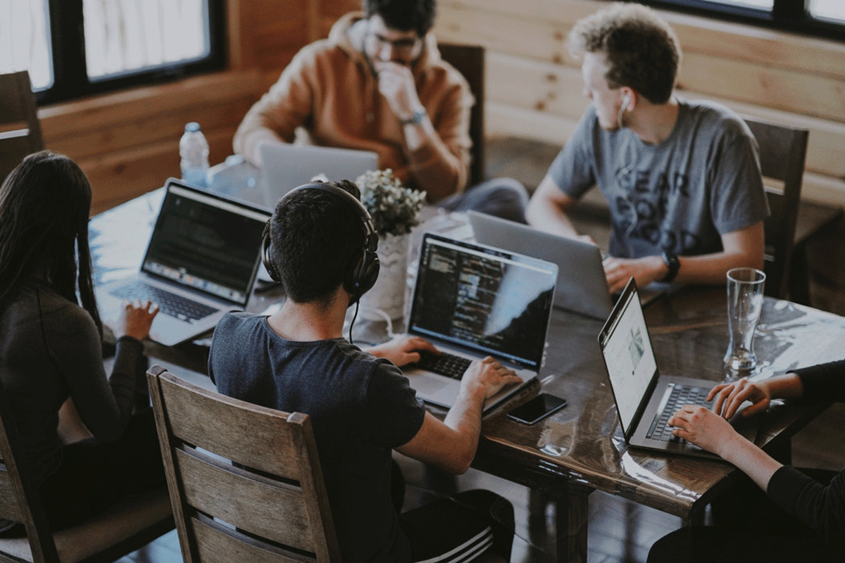 A diverse group of individuals gathered around a table, engrossed in their work on laptops.