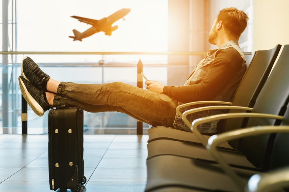 A man seated, feet raised, suitcase before him and see the aeroplane