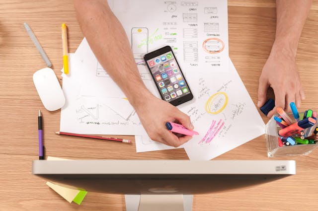 A person using a cell phone on a desk, engrossed in their device, multitasking efficiently.