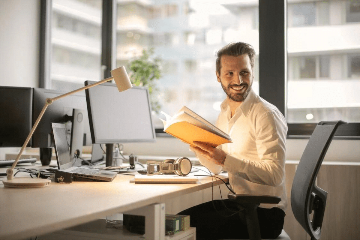 a person sitting at a desk holding a book