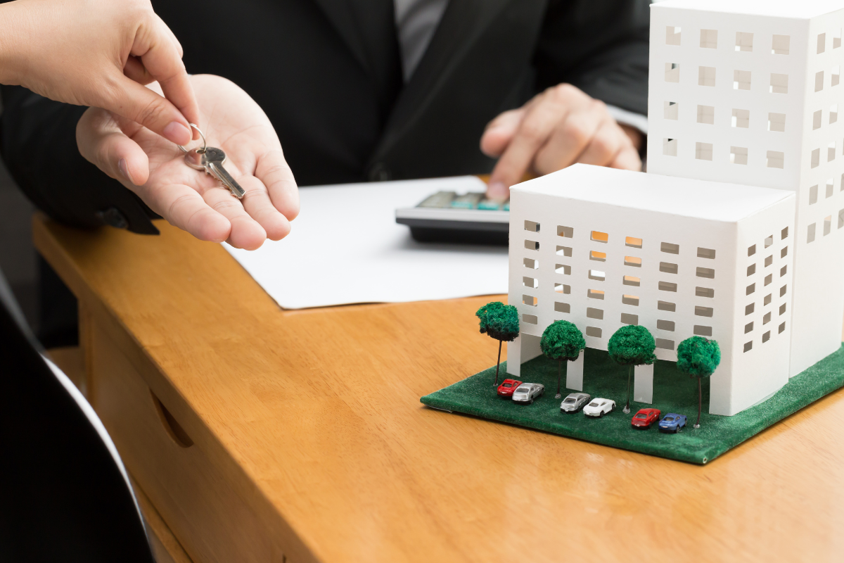 someone handing over a key next to a condo building model